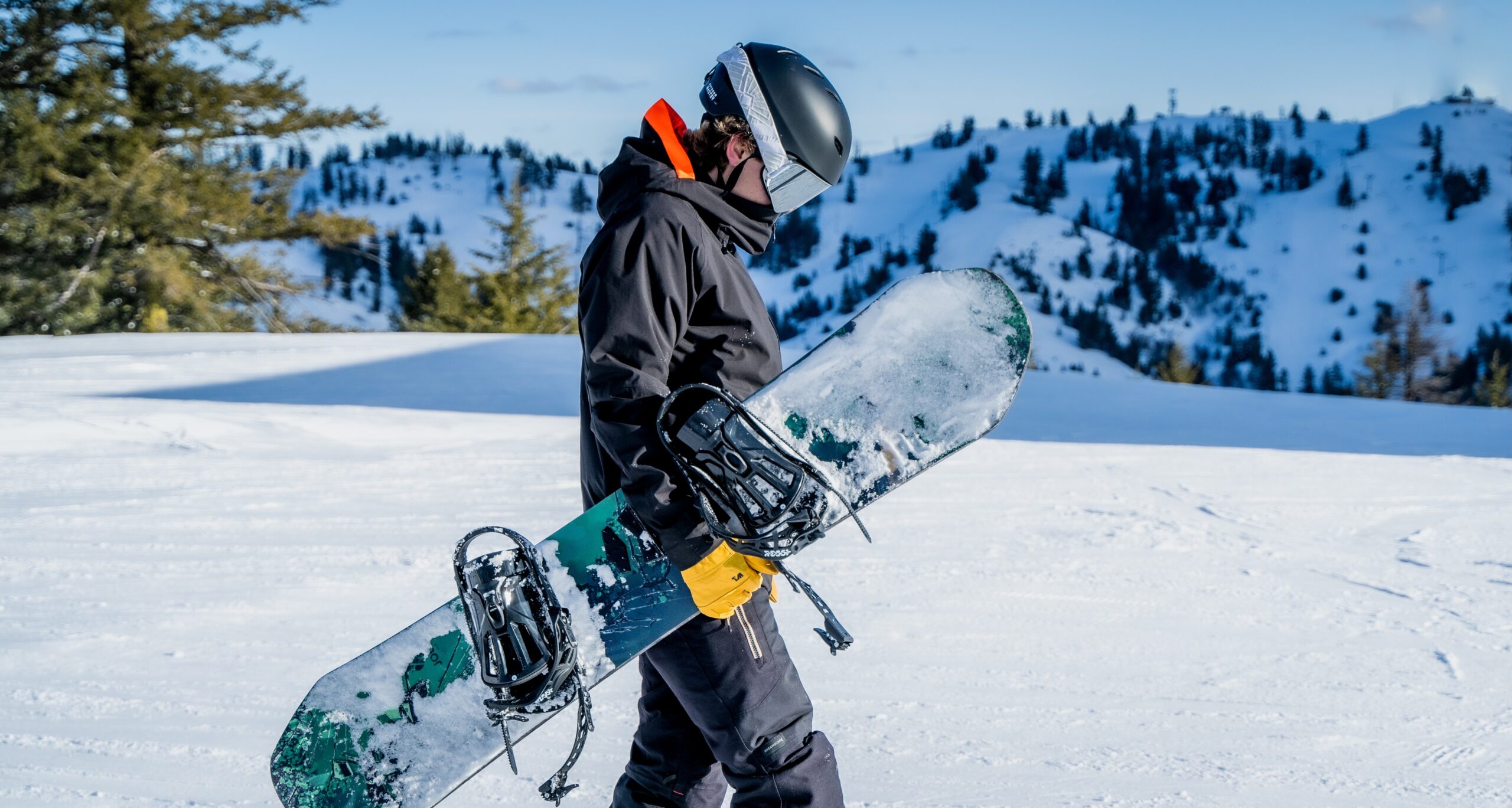 Person walking with a snowboard after learning how to choose ski gloves​ and how to choose snowboard gloves​.